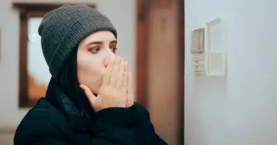 Woman Looking at her Thermostat Feeling Cold at Home