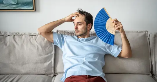 Man  sitting on a sofa while feeling extremely hot.